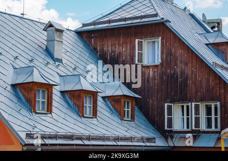 Banska Stiavnica, Slowakei - 14. August 2021: Blick auf altes Holzdach und Fassade, Fenster und Kamin. Historische Architekturdetails. Stockfoto