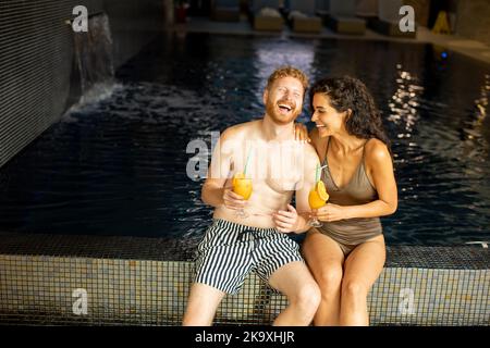 Schönes junges Paar, das sich am Pool entspannt und Orangensaft trinkt Stockfoto