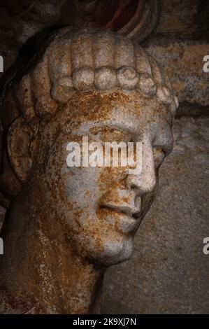 Das Gesicht des Heiligen Stephen, des ersten christlichen Märtyrers, gesteinigt, nachdem er seine Richter verurteilt hatte. Nähere Details der romanischen Säulenstatue Ende 1100s im Nordportal der Basilika Saint-Just, geweiht im Jahr 1200 in Valcabrère in Occitanie, Südwestfrankreich. Eine geformte Hauptstadt über Stephens Kopf stellt sein Märtyrertum dar. Stockfoto