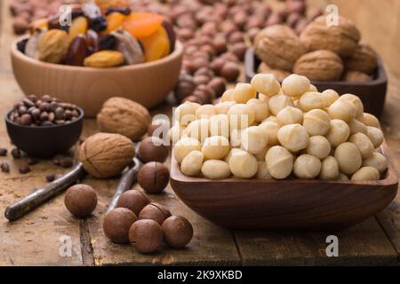 Macadamianüsse in Schale auf Holztisch geschält. Nützliche Lebensmittel für Vegetarier und Veganer. Stockfoto