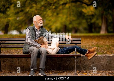 Der gutaussehende Großvater verbringt am Herbsttag Zeit mit seiner Enkelin auf der Bank im Park Stockfoto