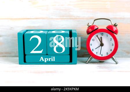 April 28. Blauer Kubuskalender mit Monat und Datum und rotem Wecker auf Holzhintergrund Stockfoto