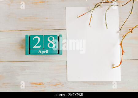 April 28. Blauer Würfelkalender mit Monat und Datum und weißem Mockup-Rohling auf Holzhintergrund Stockfoto