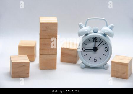 Leere Holzwürfel und weißer Wecker auf weißem Hintergrund mit anpassbarem Platz für Text oder Ideen. Stockfoto