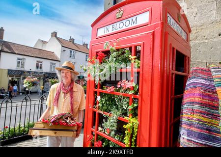 Schmuck und indische Textilien Stallholder Dan Crane mit einer Telefonbox, die für „G in Bloom“ im Market Place, Glastonbury in Somerset gepflanzt wurde Stockfoto