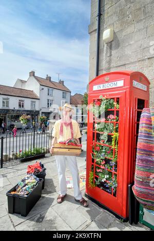 Schmuck und indische Textilien Stallholder Dan Crane mit einer Telefonbox, die für „G in Bloom“ im Market Place, Glastonbury in Somerset gepflanzt wurde Stockfoto