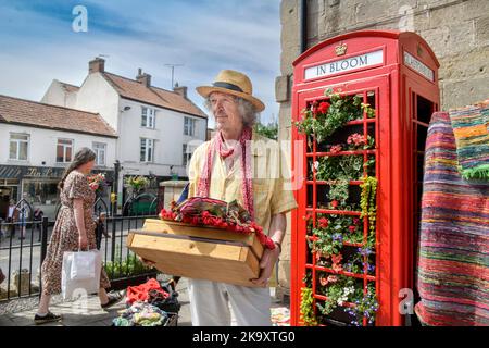 Schmuck und indische Textilien Stallholder Dan Crane mit einer Telefonbox, die für „G in Bloom“ im Market Place, Glastonbury in Somerset gepflanzt wurde Stockfoto