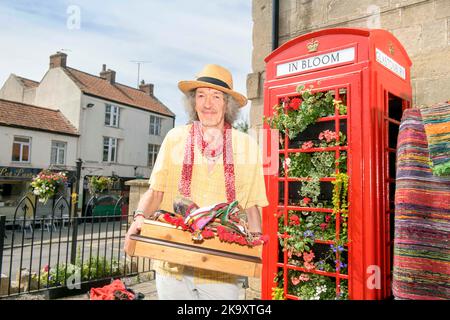 Schmuck und indische Textilien Stallholder Dan Crane mit einer Telefonbox, die für „G in Bloom“ im Market Place, Glastonbury in Somerset gepflanzt wurde Stockfoto