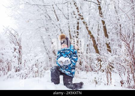 Junge, der an sonnigen Wintertagen Schnee in die Luft wirft, Rückansicht Stockfoto