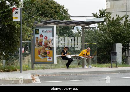 Barcelona, Spanien - 23. Oktober 2022: Mann und Frau, die im Handy aufgehen, während sie auf den Bus warten, Fast-Food-Werbung auf der Busstr Stockfoto
