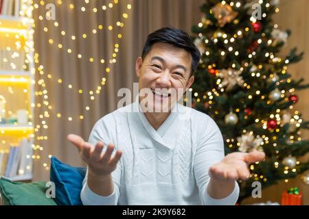 Nahaufnahme Foto Webcam Ansicht des glücklichen asiatischen Mann zu Hause Blick auf die Kamera und lächeln wünschen Freunden und Familie Frohe Weihnachten und Neujahr, Videoanruf und Online-Grüße. Stockfoto