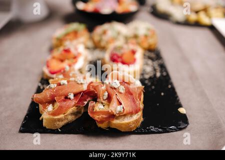 Köstliche Bruschetta mit Prosciutto und Gorgonzola auf schwarzem Steinbrett im Restaurant. Feiern Stockfoto