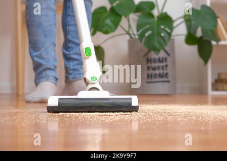 Reinigungsraum mit modernem kabellosem Staubsauger ohne Kabel. Mann in Jeans putzt den Boden mit einem modernen Akku-Staubsauger ohne Kabel. Der Mann entfernt Sägespäne mit dem Staubsauger vom Boden. Stockfoto