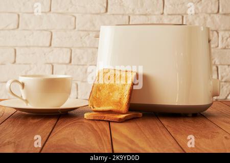 Frühstück mit heißem Kaffeebecher, geröstetem Brot und Toaster auf dem Holztisch. Kochen und Haushaltswaren Technologien Hintergründe Stockfoto