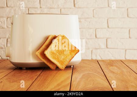 Weißer elektrischer Toaster und geröstete Brotscheiben in der modernen Küche. Kochen und Haushaltswaren Technologien Hintergründe Stockfoto