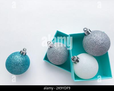 Nahaufnahme von türkisfarbenen Schmuckkisten, in deren Innenseite eine glänzende Weihnachtskugeln in Weiß, Blau und Silber auf der rechten Seite zu sehen ist. Weißer Hintergrund. Stockfoto