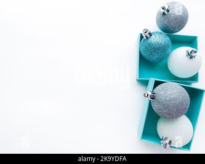 Türkisfarbene Schmuckkisten, in deren Innenseite eine glänzende Weihnachtskugeln in Weiß, Blau und Silber auf der rechten Seite zu sehen ist. Weißer Hintergrund. Speicherplatz kopieren. Stockfoto