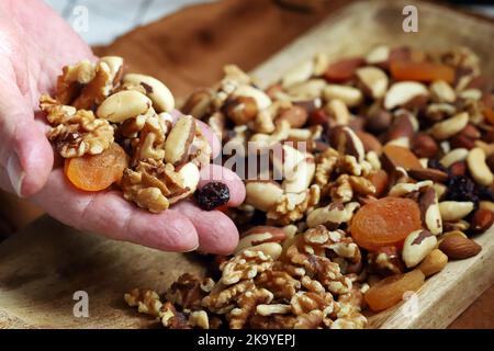 Eine Handvoll Nüsse und getrocknete Früchte in männlichen Handflächen. Gesunde Süßigkeiten oder Snacks. Stockfoto