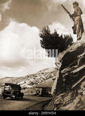 Afghanistan - Ein Foto aus den 1940er Jahren eines bewaffneten Stammesanmannes, der als britischer Konvoi in Waziristan ( وزیرستان) auf der Straße nach Razmak beobachtet wurde. (رزمک -- 1940 کی دہائی کی ایک تصویر جس میں ایک مقامی مسلح قبائ میں برطانوی قافلے کے طور پر رزمک جانے والی سڑک پر نظر رکھے ہوئے ہے۔ -- د ۱۹۴۰ کال د یوه سیمه ایز وسله وال قوم انځور چې په وزیرستان کې د بریتانیا د کاروان په توګه څارل شوی وو . Stockfoto