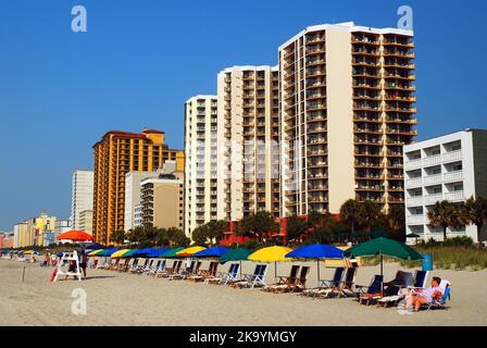 Am frühen Morgen, vor den Massen, werden Sonnenschirme und Sitzplätze am Myrtle Beach vor den Hochhäusern und Apartmentgebäuden angeordnet Stockfoto