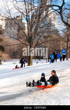 Ein Vater und ein Sohn genießen die gemeinsame Zeit mit der Familie an einem Schneetag und fahren auf dem Pilgrim Hill im Central Park von New York City Stockfoto