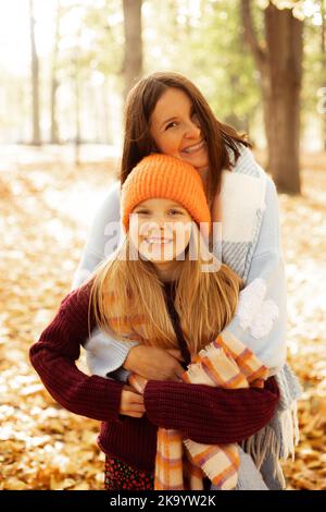 Portrait von fröhlichen Frau und Mädchen mit Liebe kuscheln einander isoliert auf sonnigen gelben Wald Hintergrund. Glückliche Mutter und Tochter im gemütlichen Herbst Stockfoto