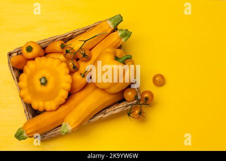 Set aus gelbem Gemüse in einem Weidenkorb. Speicherplatz kopieren. Flach liegend. Gelber Hintergrund. Stockfoto