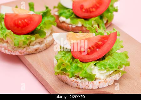 Reiskuchen-Sandwiches mit Tomaten, Salat und Ei auf Holzbrett. Einfaches Frühstück. Diät-Essen. Schnelle und gesunde Sandwiches. Knäckebrot mit leckerer Füllung. Gesunder Ernährungs-Snack Stockfoto