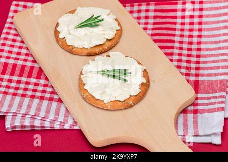 Knuspriges Cracker Sandwich mit Frischkäse und Rosmarin auf Holzkochbrett auf Magenta Hintergrund Stockfoto