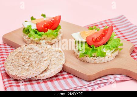 Reiskuchen-Sandwiches mit Tomaten, Salat und Ei auf Holzbrett. Einfaches Frühstück. Diät-Essen. Schnelle und gesunde Sandwiches. Knäckebrot mit leckerer Füllung. Gesunder Ernährungs-Snack Stockfoto