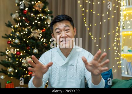 Nahaufnahme Foto Webcam Ansicht des glücklichen asiatischen Mann zu Hause Blick auf die Kamera und lächeln wünschen Freunden und Familie Frohe Weihnachten und Neujahr, Videoanruf und Online-Grüße. Stockfoto