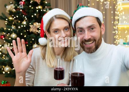 Familie in der Liebe Paar Mann und Frau zusammen für Weihnachten Gruß Freunde sprechen aus der Ferne auf Video-Anruf Blick auf Smartphone-Kamera in Weihnachtsmann Hüte mit Gläsern Wein, Online-Grüße. Stockfoto