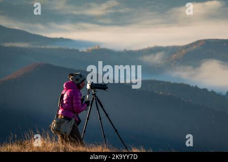 Reisefotograf bei der Arbeit. Fotografin mit professionellem Stativ und Kamera macht Fotos hoch in den Bergen Stockfoto