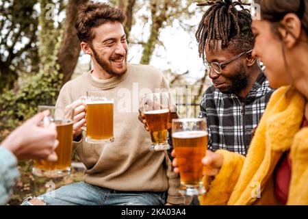 Eine multiethnische Gruppe junger Freunde, die im Waldpub eine Party machen, sich unterhalten und Bier trinken - Alkoholgetränk, Vielfalt, Wohlbefinden und pe Stockfoto