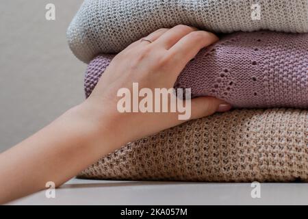Nahaufnahme einer weiblichen Hand, die einen Pullover mit einem Stapel gefalteter Strickwaren ergreift Stockfoto