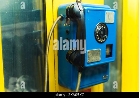 Altmodische, hellgelbe Telefonzelle mit dunkelblauem Telefon. Die Entwicklung von Technologie und Kommunikationssystemen. Hochwertige Fotos Stockfoto