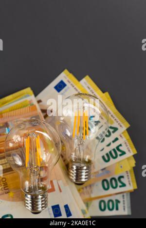 Stromrechnungen bezahlen. Stromkosten. Stromrechnungen bezahlen. Glühbirnen und Euro-Banknoten auf grauem Hintergrund. Energiekrisen Stockfoto