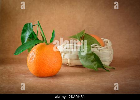 Orange mit einem Ast und Blättern auf einem dunkelbeigen Hintergrund in einem horizontalen Format Stockfoto