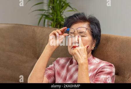 Ältere asiatische Frau, die eine Brille auszieht und an einem Syndrom mit trockenen Augen leidet Stockfoto