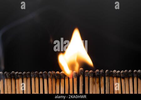 Reihen brennender Streichhölzer mit Flammen aus nächster Nähe. Blick auf die Spiele, während sie brennen und rauchen. Aufnahme von Zündhölzern gegen schwarzen Hintergrund. Stockfoto
