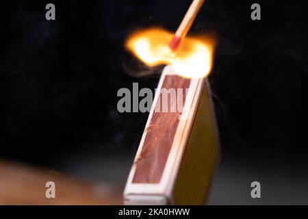 Streichholzschachtel feuert in Zeitlupe in Nahaufnahme auf Streichholzschachtel. Das Spiel wurde angezündet, ein loderndes Feuer. Aufnahme des Zündungs-Matches gegen schwarzen Hintergrund. Stockfoto