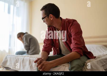 Verwirrt Mann schaut zu weinen Mädchen sitzt auf der gegenüberliegenden Seite des Bettes nach unangenehmen Gespräch Stockfoto