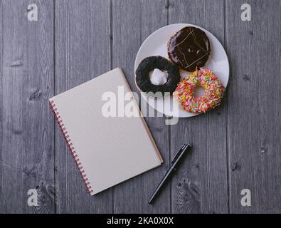 Draufsicht auf Notizbuch, Kugelschreiber und Donut auf Holzhintergrund Stockfoto