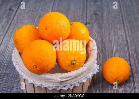 Korb mit Orangen auf Holzhintergrund Stockfoto