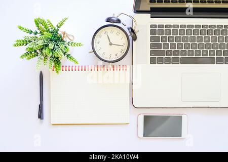 Flach Lay Draufsicht auf weißen Tisch mit Notebook, ein Stift, Smartphone und grüne Pflanze Stockfoto