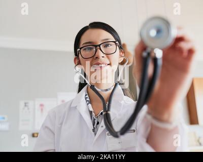 Eine junge Ärztin, die sich mit einem Stethoskop ausstreut, um Ihrem Herzschlag zuzuhören. Stockfoto