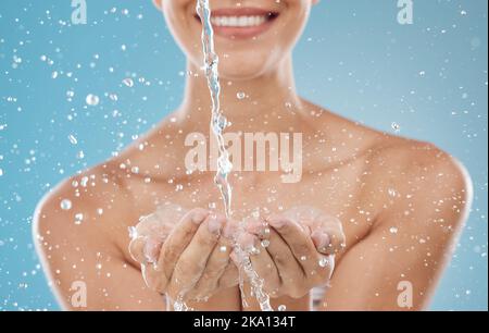 Hautpflege, Wasser und Hände auf blauem Hintergrund im Studio zur Hydratation, Erfrischung und Gesichtsreinigung. Splash, Wellness und Frau bereit, Gesicht zu reinigen Stockfoto