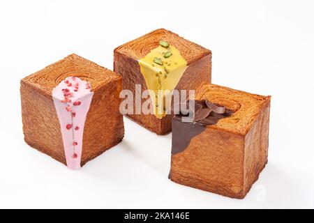 Drei würfelförmige Croissants mit cremiger Beerenglasur, Pistazien-Sauce und Schokoladenganache Stockfoto