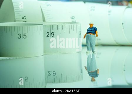 Miniaturfigur eines übergewichtigen Mannes gegen Maßband. Stockfoto