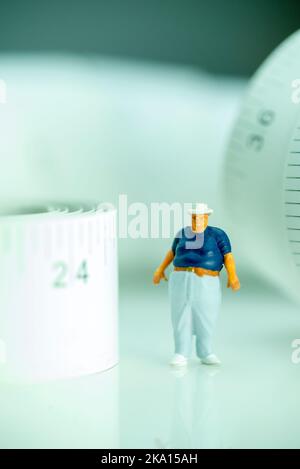 Miniaturfigur eines übergewichtigen Mannes gegen Maßband. Stockfoto